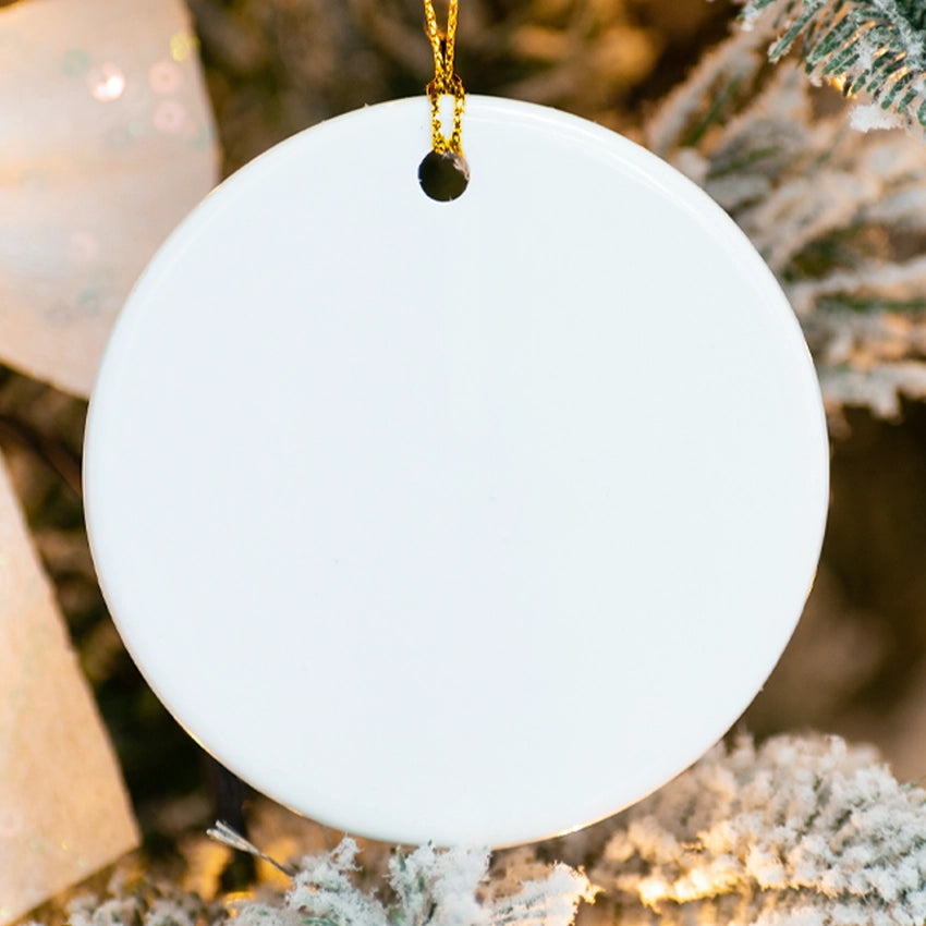 White round ornament hanging on a tree with blurred lights and greenery in the background
