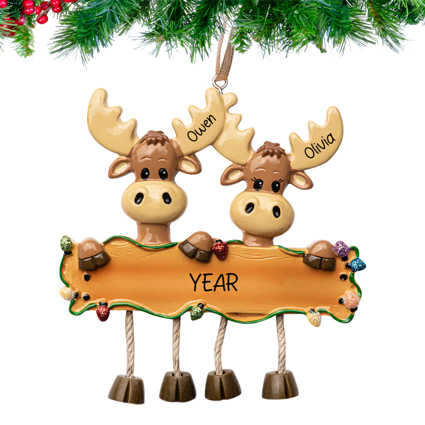 Personalized moose couple Christmas ornament with a heart above them, hanging from a decorated evergreen branch.