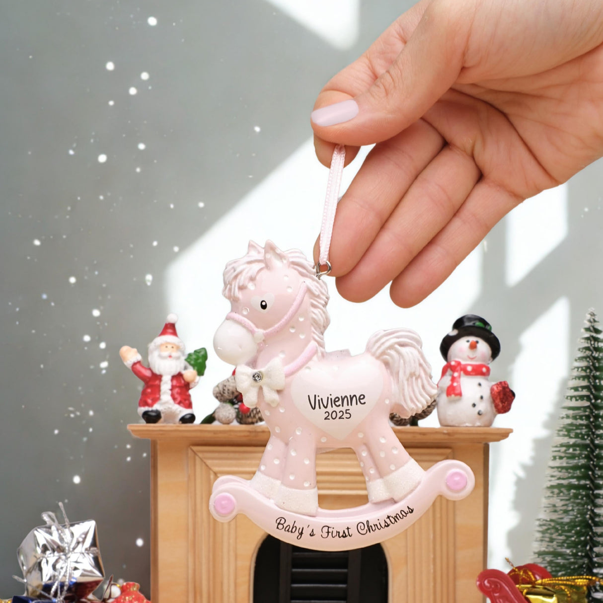Pink rocking horse ornament with 'Baby's First Christmas' text, held by a hand in a festive setting.