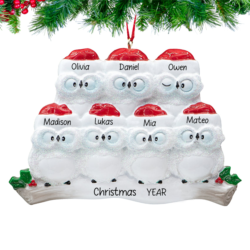 owl parents with five owlets on a snowy branch, ornament personalized with seven names and 2025, hanging on a festive Christmas tree.