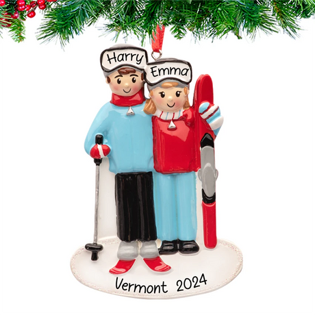 Skiing couple ornament with names and 2025 engraved, skiing down a snowy hill on a decorated Christmas tree branch.