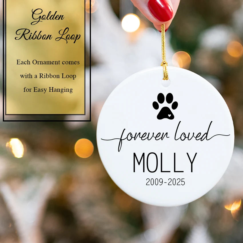 White ornament with black paw print ' against a blurred Christmas tree background.