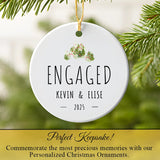 Engaged couple ornament hanging on Christmas tree with jungle leaf motif and gold ribbon