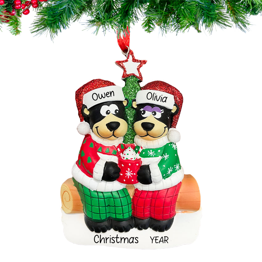 Personalized black bear couple ornament with a heart and custom names, hanging from a snow-dusted pine branch