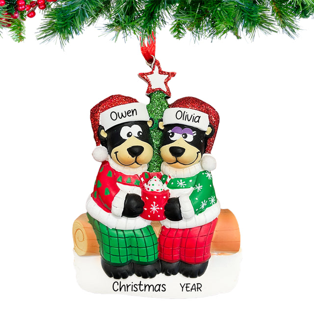 Personalized black bear couple ornament with a heart and custom names, hanging from a snow-dusted pine branch