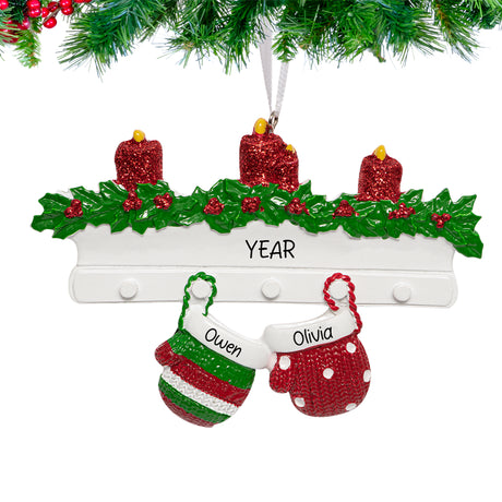  Two linked Christmas mittens ornament personalized with names and year, hanging from a snow-dusted pine branch