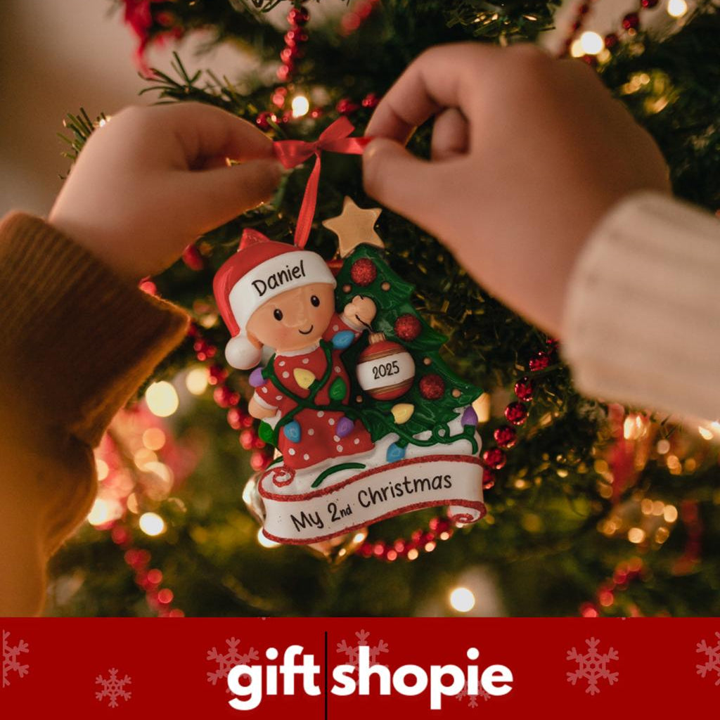 Person hanging a personalized Christmas ornament on a tree with 'gift shopie' branding.