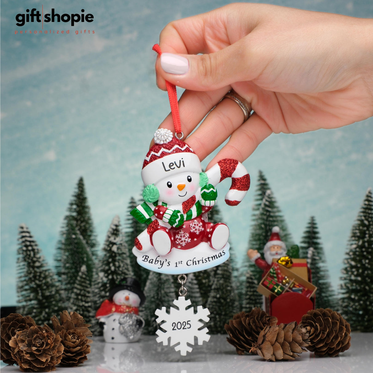 Personalized Christmas ornament with 'Baby's 1st Christmas 2025' text, held by a hand against a festive background.